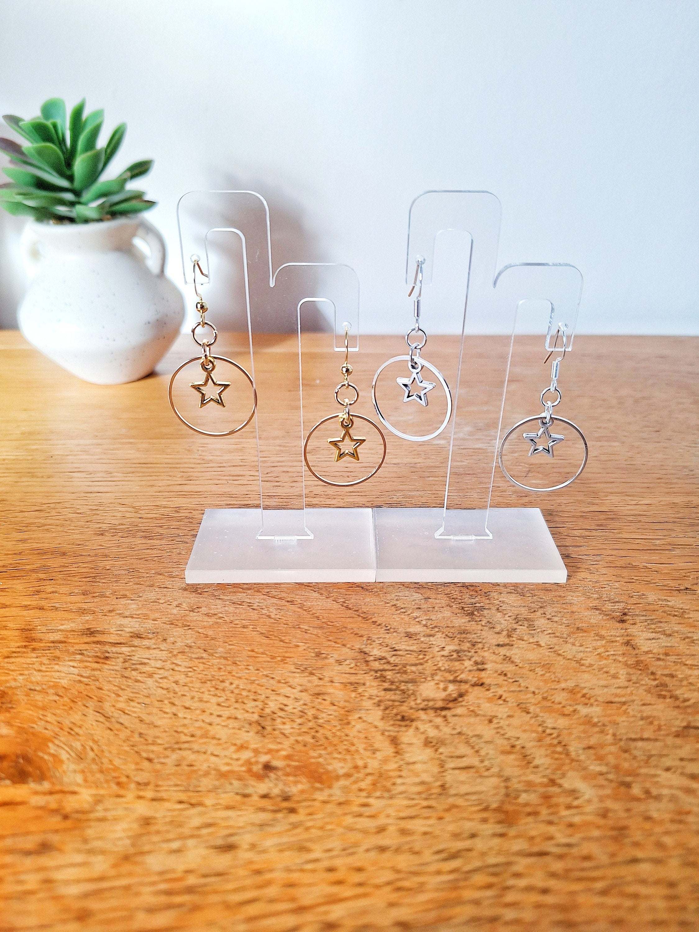 Vega Star Earrings in silver and gold, featuring hollow stars within a 25mm circle, displayed on a stand.