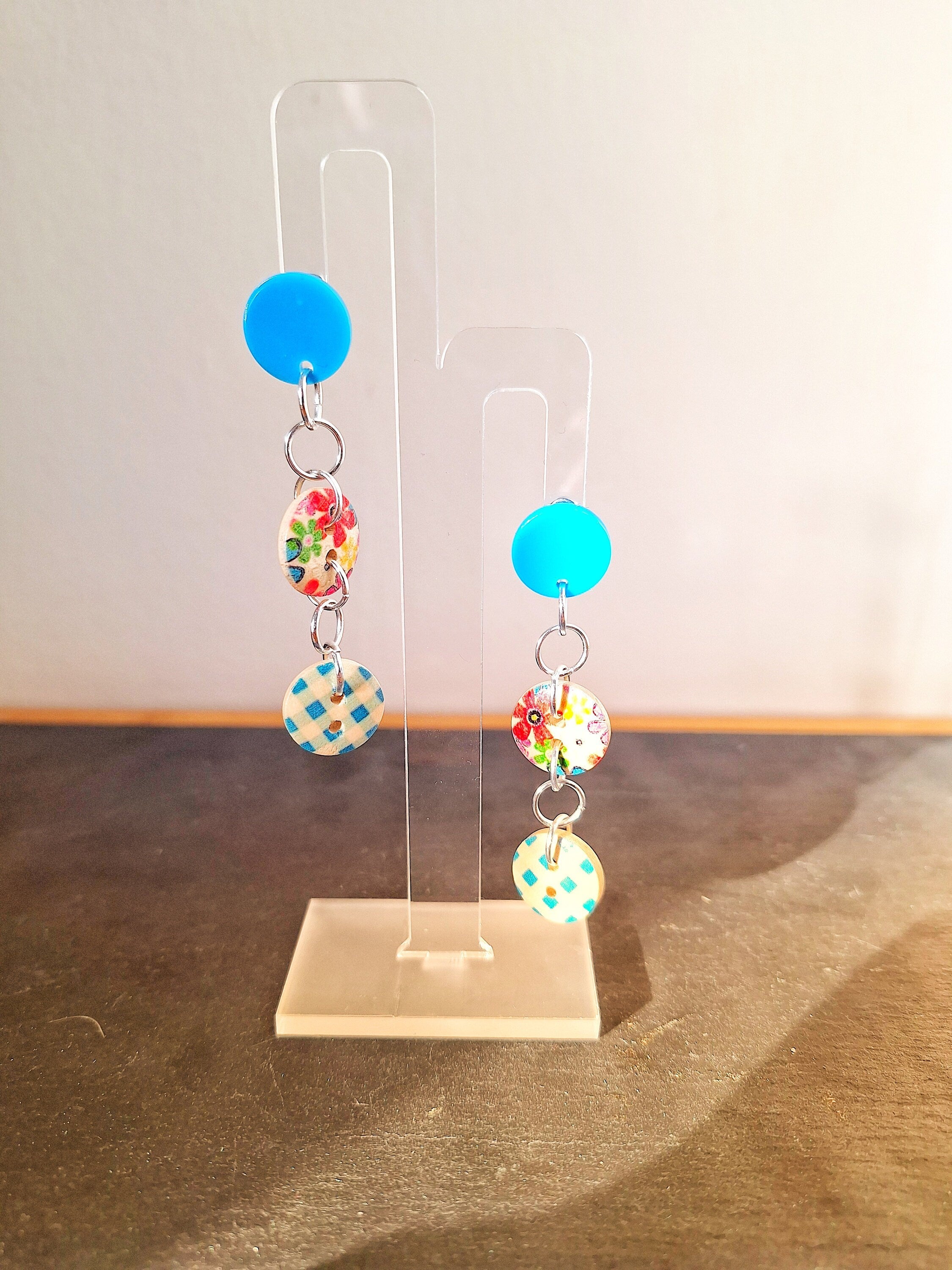 Bella Button Earrings in blue and pink with wooden buttons and acrylic discs on display stand.