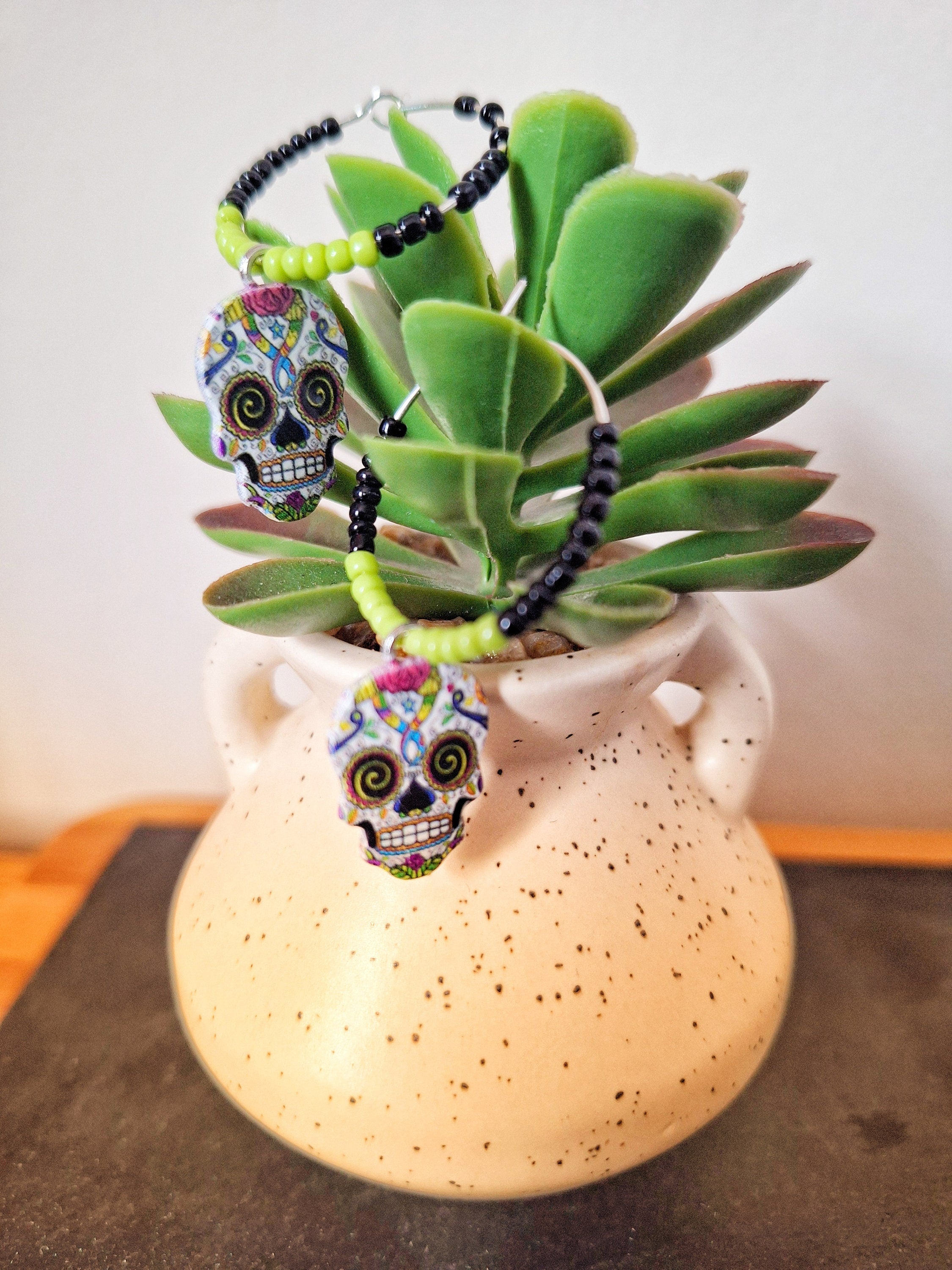 Calavera Hoop Earrings with colorful skull charms and glass seed beads in a pot.