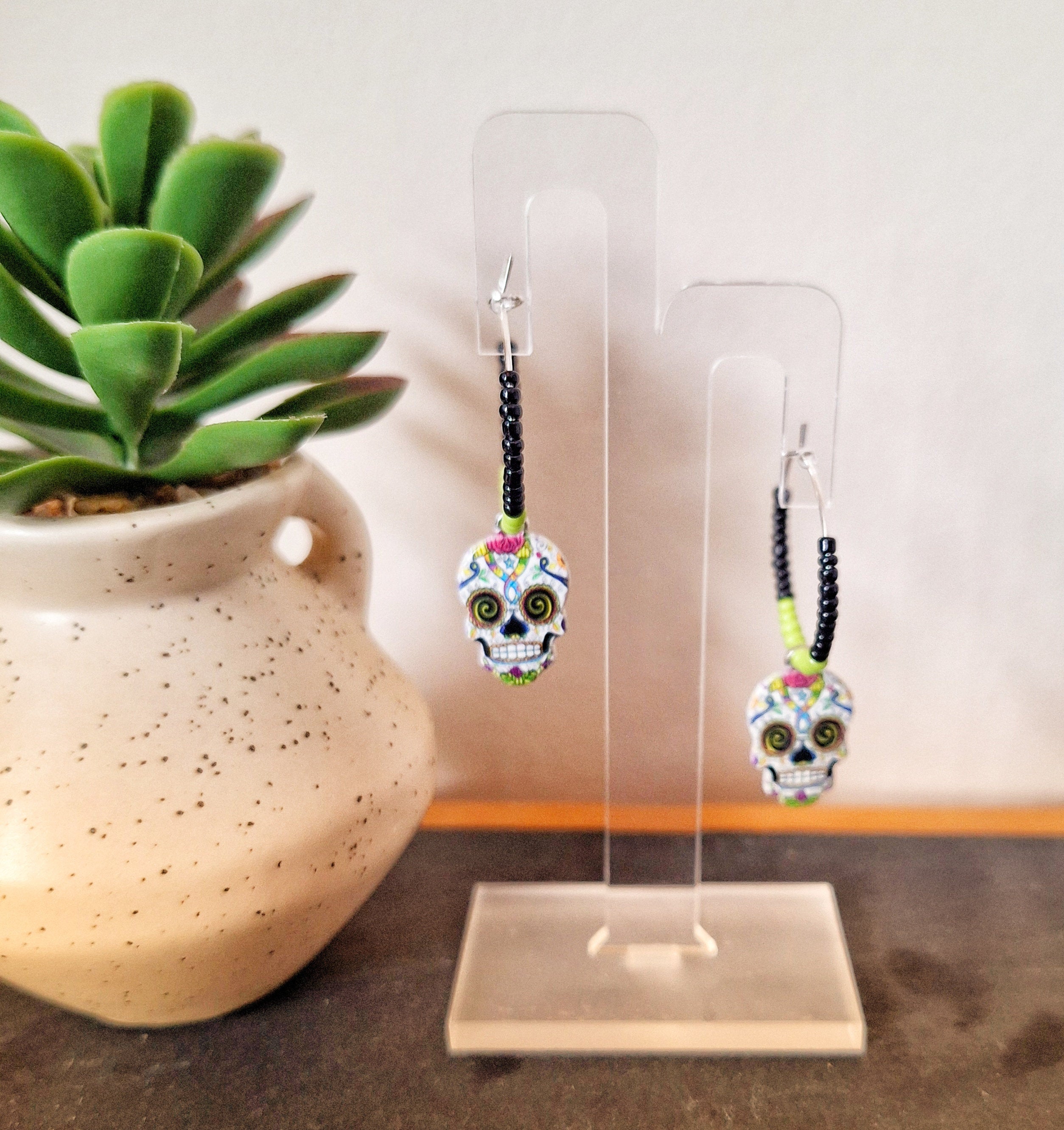 Calavera hoop earrings with skull charms and glass seed beads in an acrylic display.