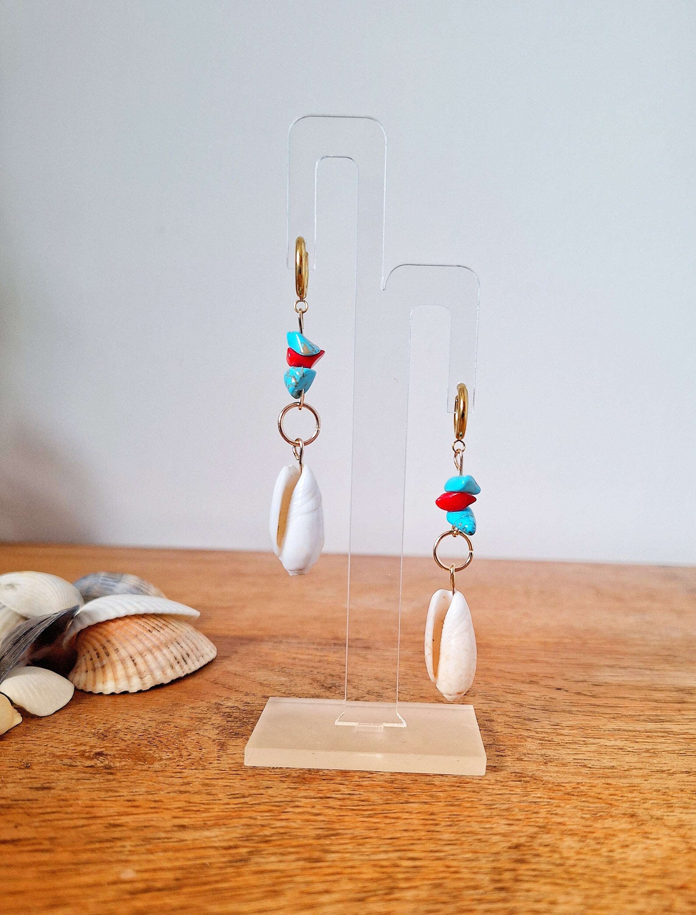Ariel turquoise and coral shell earrings on display stand with conch shells nearby.